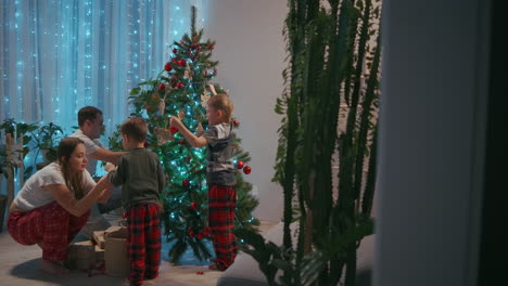 Happy-family-preparing-for-New-Year-winter-holidays-celebration-concept.-Young-30s-couple-his-preschool-adorable-two-sons-decorating-Christmas-tree-create-festive-mood-atmosphere-at-modern-cozy-house.-High-quality-4k-footage